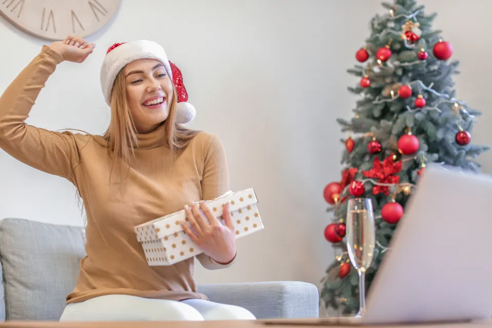 Woman opening a holiday gift in front of a laptop